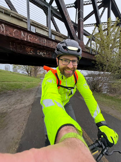 Smiling cyclist in a high-visibility jacket under a bridge